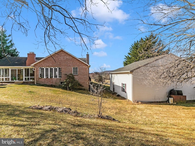 back of house featuring a yard, brick siding, a chimney, and a sunroom