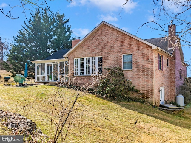 rear view of house with a lawn, brick siding, a chimney, and a sunroom