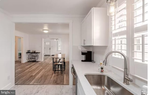kitchen featuring stainless steel dishwasher, a sink, white cabinetry, and crown molding