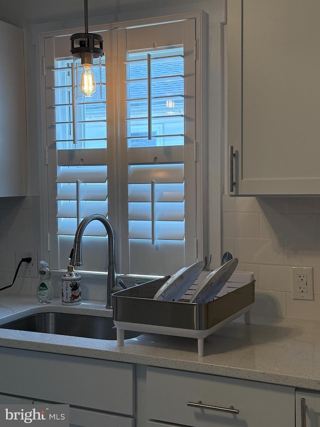 kitchen featuring a sink, light stone counters, white cabinets, and tasteful backsplash