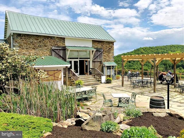 back of property featuring a pergola, stone siding, a standing seam roof, a patio, and metal roof