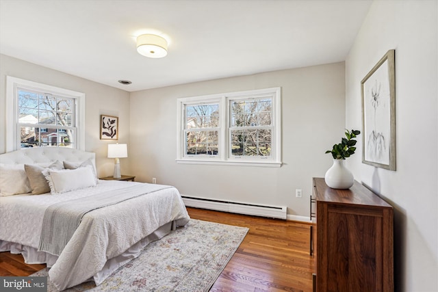 bedroom with multiple windows, a baseboard heating unit, baseboards, and hardwood / wood-style flooring