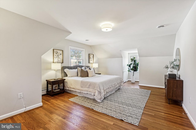 bedroom featuring wood finished floors, visible vents, baseboards, vaulted ceiling, and a baseboard heating unit