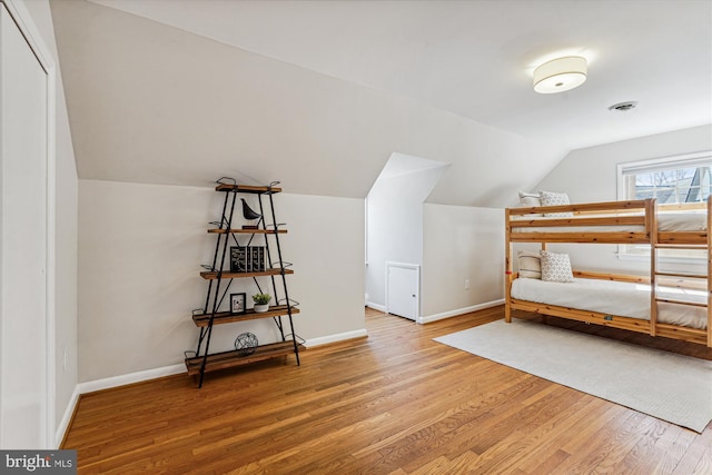 bedroom with visible vents, baseboards, lofted ceiling, and wood finished floors