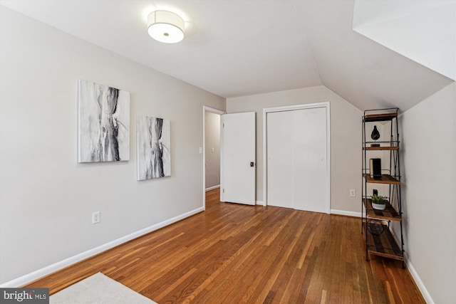 unfurnished bedroom with a closet, lofted ceiling, baseboards, and hardwood / wood-style flooring