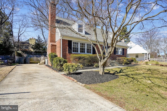 cape cod home featuring brick siding, fence, a front yard, a chimney, and driveway