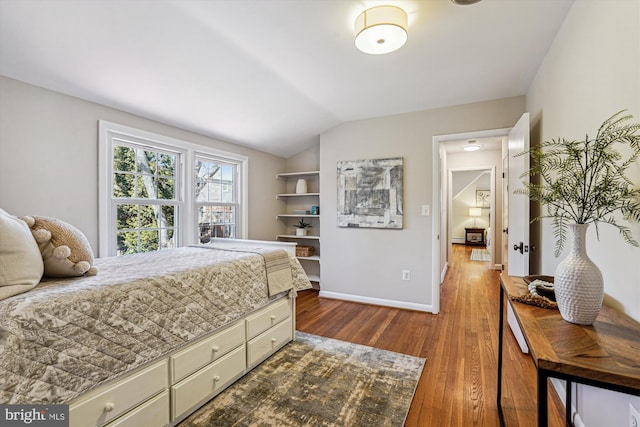 bedroom with baseboards, lofted ceiling, and wood finished floors