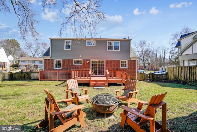 back of house featuring a wooden deck, a fenced backyard, a fire pit, a lawn, and brick siding