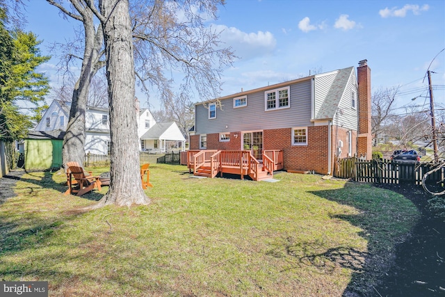 back of house with brick siding, fence private yard, a chimney, a yard, and a deck