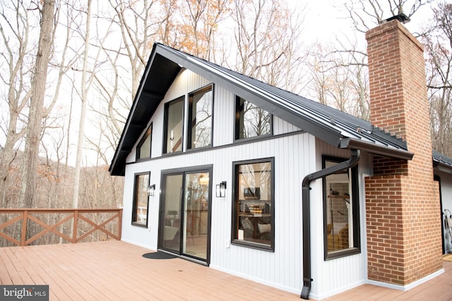 exterior space with a chimney, metal roof, a standing seam roof, a wooden deck, and brick siding