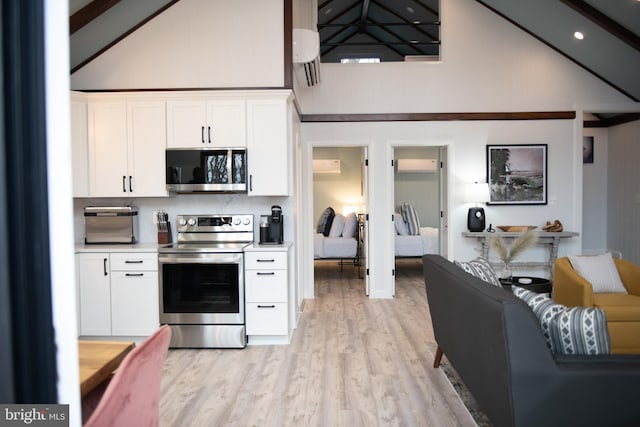 kitchen with high vaulted ceiling, white cabinets, light countertops, appliances with stainless steel finishes, and light wood-type flooring