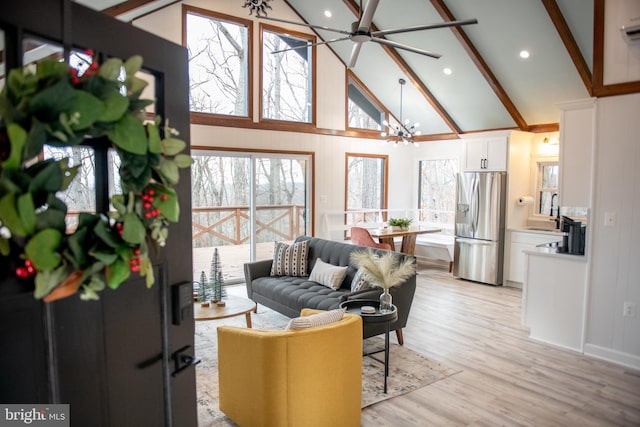 living area with high vaulted ceiling, beam ceiling, light wood-style flooring, and ceiling fan with notable chandelier