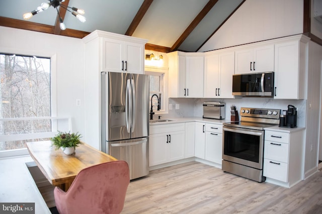 kitchen with vaulted ceiling with beams, white cabinetry, appliances with stainless steel finishes, and a sink