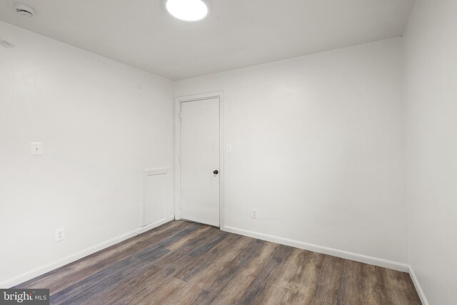 spare room with baseboards and dark wood finished floors