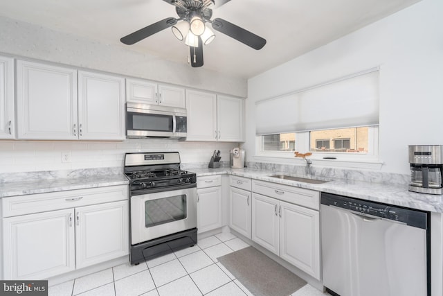 kitchen featuring light tile patterned floors, tasteful backsplash, appliances with stainless steel finishes, white cabinets, and a sink