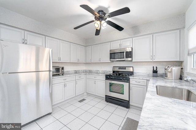 kitchen with light tile patterned floors, appliances with stainless steel finishes, a sink, and white cabinets