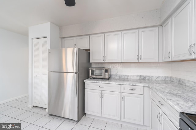 kitchen with light tile patterned floors, a toaster, backsplash, and freestanding refrigerator