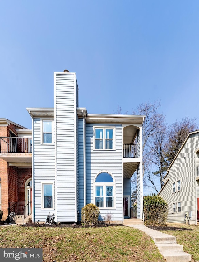 view of property with a chimney, a balcony, and a front lawn