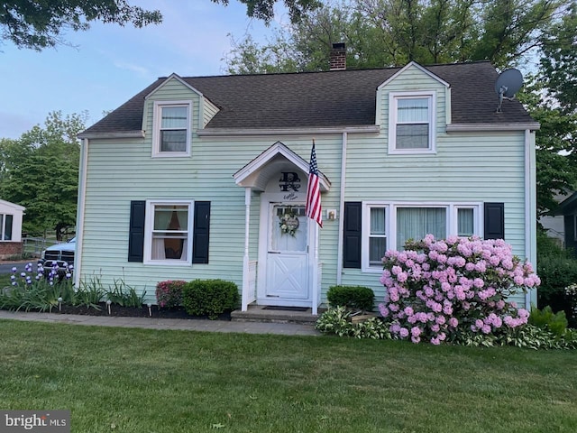 view of front facade with a front lawn, a chimney, and a shingled roof