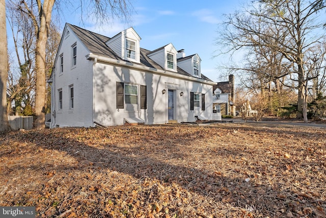 cape cod house featuring a chimney and brick siding