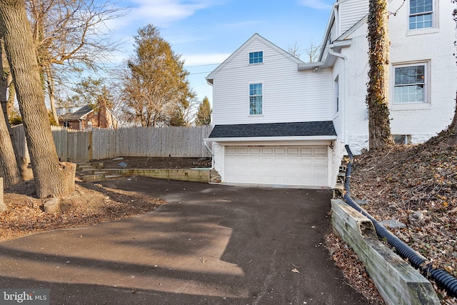 view of side of home with driveway, roof with shingles, an attached garage, and fence