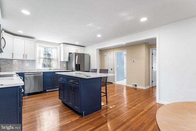 kitchen with appliances with stainless steel finishes, wood finished floors, blue cabinetry, and a kitchen bar