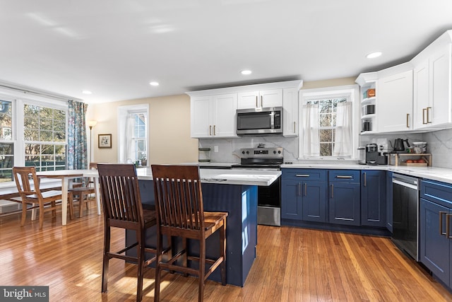 kitchen with white cabinets, appliances with stainless steel finishes, wood finished floors, light countertops, and blue cabinetry