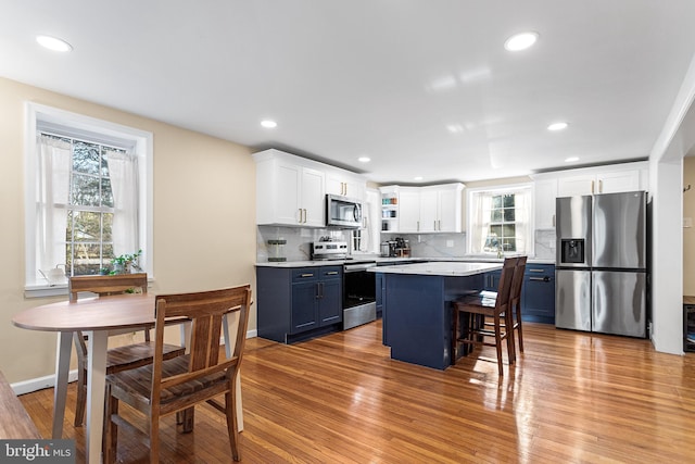 kitchen with stainless steel appliances, light wood-style floors, white cabinets, a center island, and tasteful backsplash