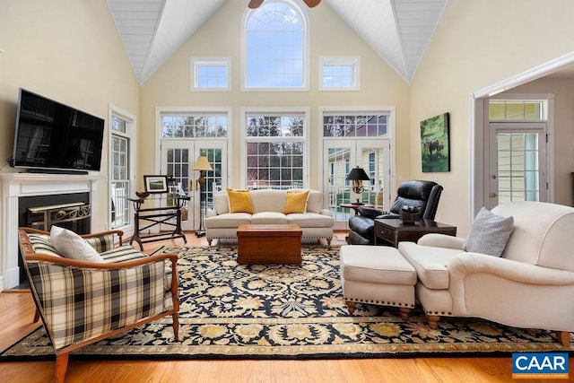 living area featuring a glass covered fireplace, high vaulted ceiling, and wood finished floors