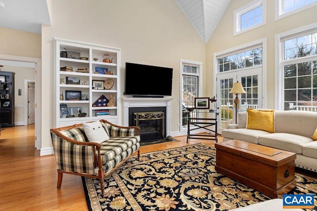 living room featuring a fireplace with flush hearth, high vaulted ceiling, light wood-type flooring, and baseboards