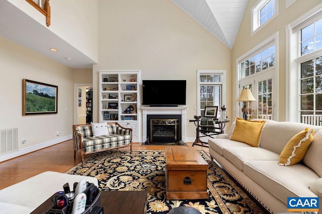 living room featuring visible vents, a fireplace with flush hearth, high vaulted ceiling, wood finished floors, and baseboards