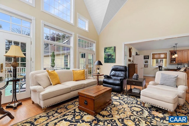 living room with light wood finished floors, high vaulted ceiling, and baseboards