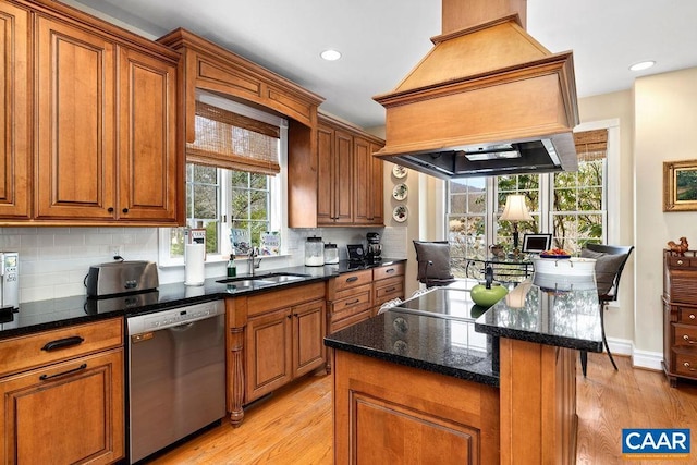 kitchen featuring premium range hood, a sink, decorative backsplash, light wood-style floors, and dishwasher