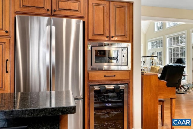 kitchen featuring wood finished floors, stainless steel appliances, wine cooler, brown cabinetry, and vaulted ceiling