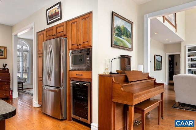 kitchen with baseboards, light wood-style flooring, stainless steel appliances, wine cooler, and brown cabinets