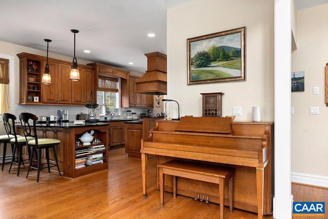 kitchen with pendant lighting, light wood-style flooring, open shelves, a kitchen breakfast bar, and dark countertops