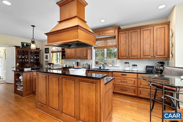 kitchen featuring brown cabinetry, light wood finished floors, a kitchen island, a sink, and backsplash