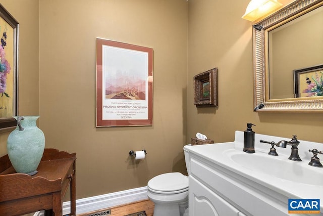 half bath with baseboards, toilet, wood finished floors, and vanity