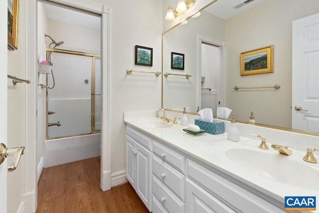 bathroom with a sink, shower / bath combination with glass door, wood finished floors, and double vanity