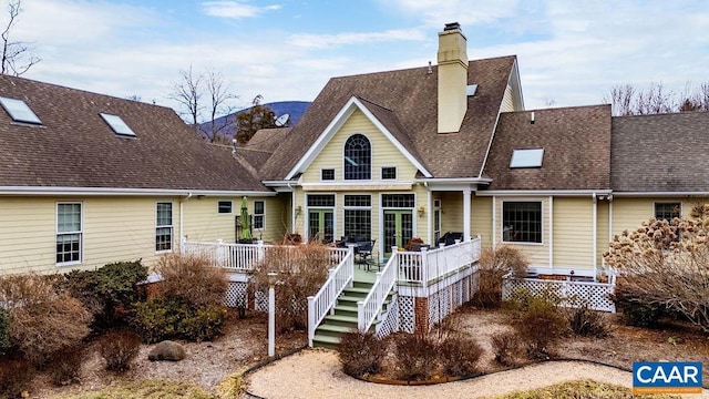 rear view of property featuring a wooden deck, stairway, a chimney, and a shingled roof