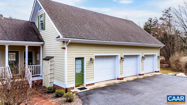 view of side of home with covered porch, a shingled roof, and a garage