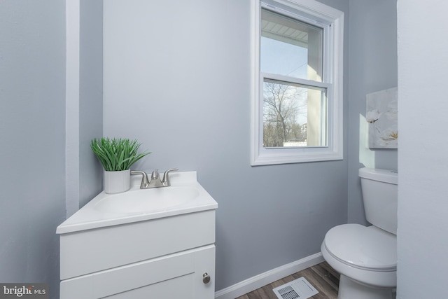 half bath with baseboards, visible vents, vanity, and toilet