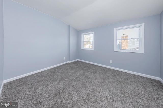 spare room with vaulted ceiling, dark colored carpet, and baseboards