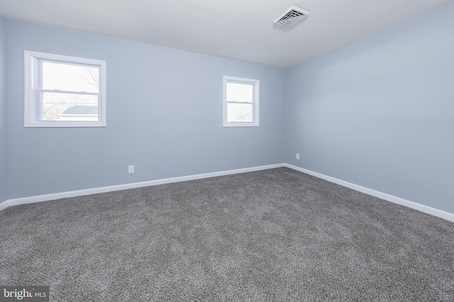 spare room with dark colored carpet, visible vents, and baseboards