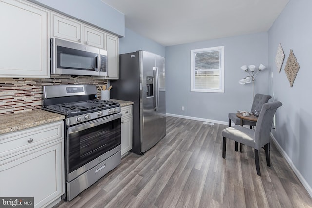 kitchen featuring appliances with stainless steel finishes, baseboards, decorative backsplash, and wood finished floors