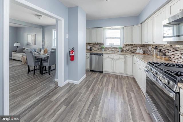 kitchen featuring stainless steel appliances, backsplash, white cabinetry, and light wood-style floors