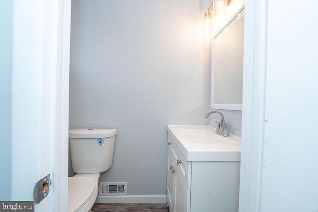 bathroom featuring visible vents, toilet, vanity, wood finished floors, and baseboards