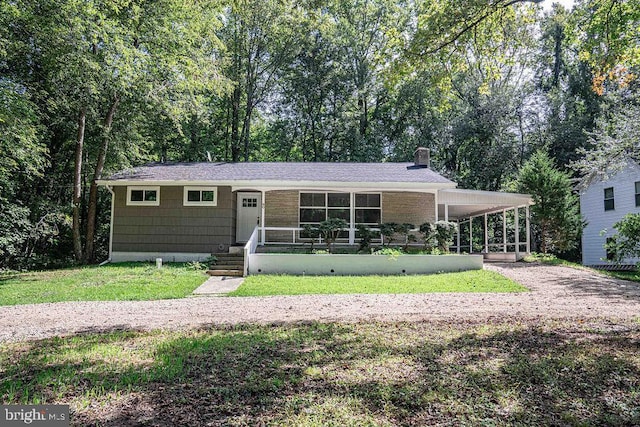 ranch-style house with a carport, a front lawn, a chimney, and gravel driveway