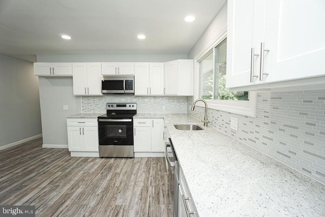 kitchen with appliances with stainless steel finishes, wood finished floors, light stone countertops, white cabinetry, and a sink