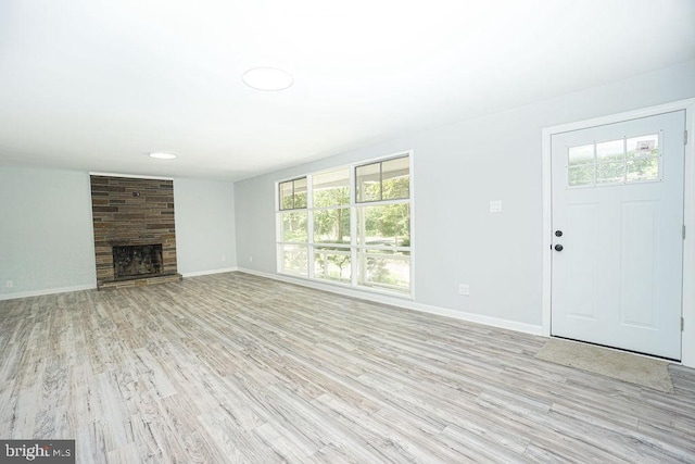 unfurnished living room with light wood-type flooring, a fireplace, and baseboards